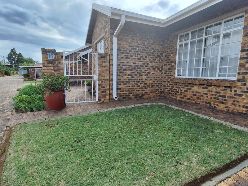 Front exterior view of a face brick townhouse featuring a paved driveway, small lawn area, and secure gated entrance.