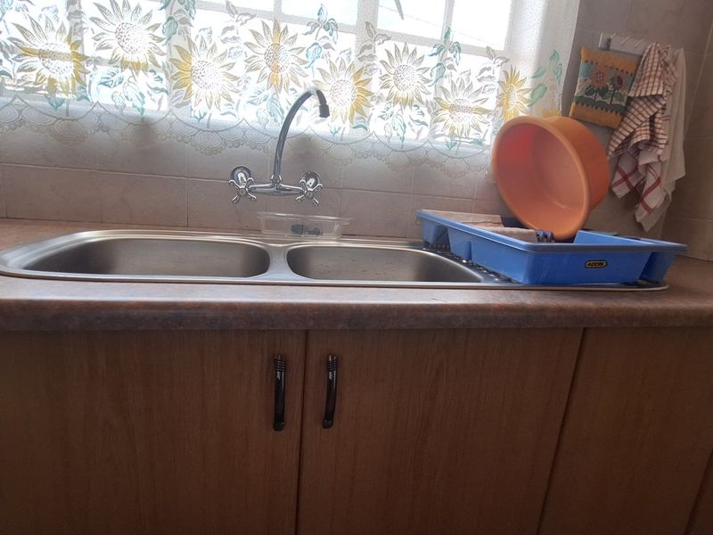 A functional kitchen sink area featuring a double bowl stainless steel sink, laminate countertops, and timber veneer cabinetry with a tiled splashback.