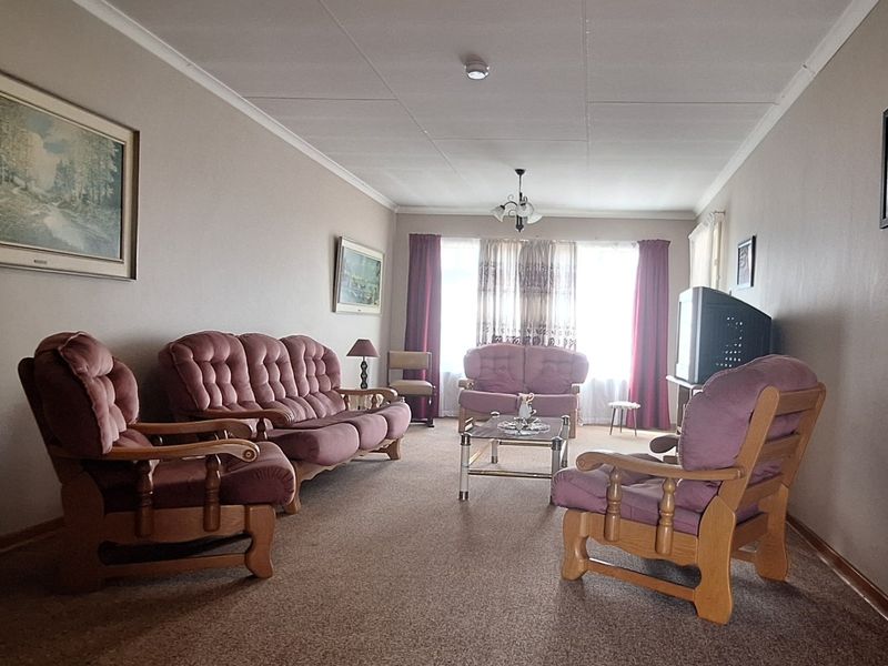 A spacious living room featuring neutral wall tones, carpeted flooring, and classic coving, offering a comfortable and functional layout for relaxation.