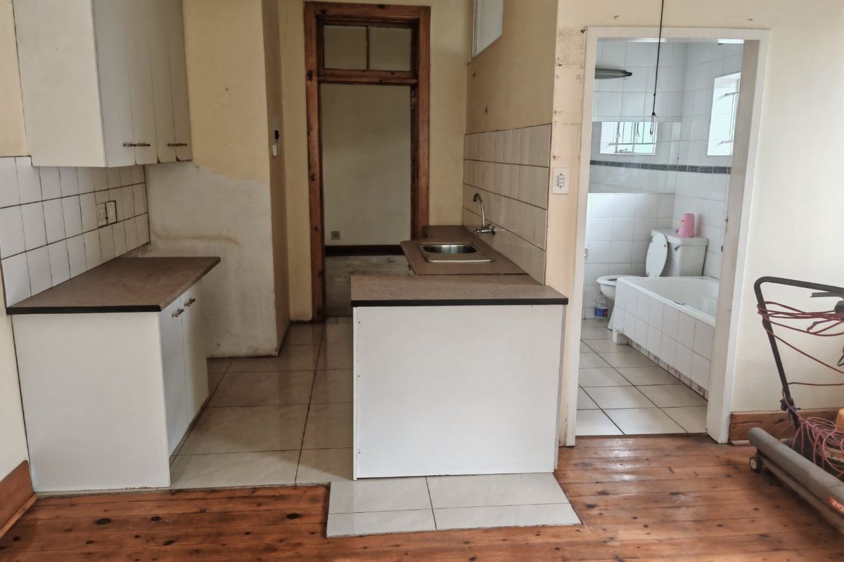A dated kitchen area featuring laminate cabinetry, tiled splashbacks, and a mix of timber and tiled flooring, requiring cosmetic updates and repairs.