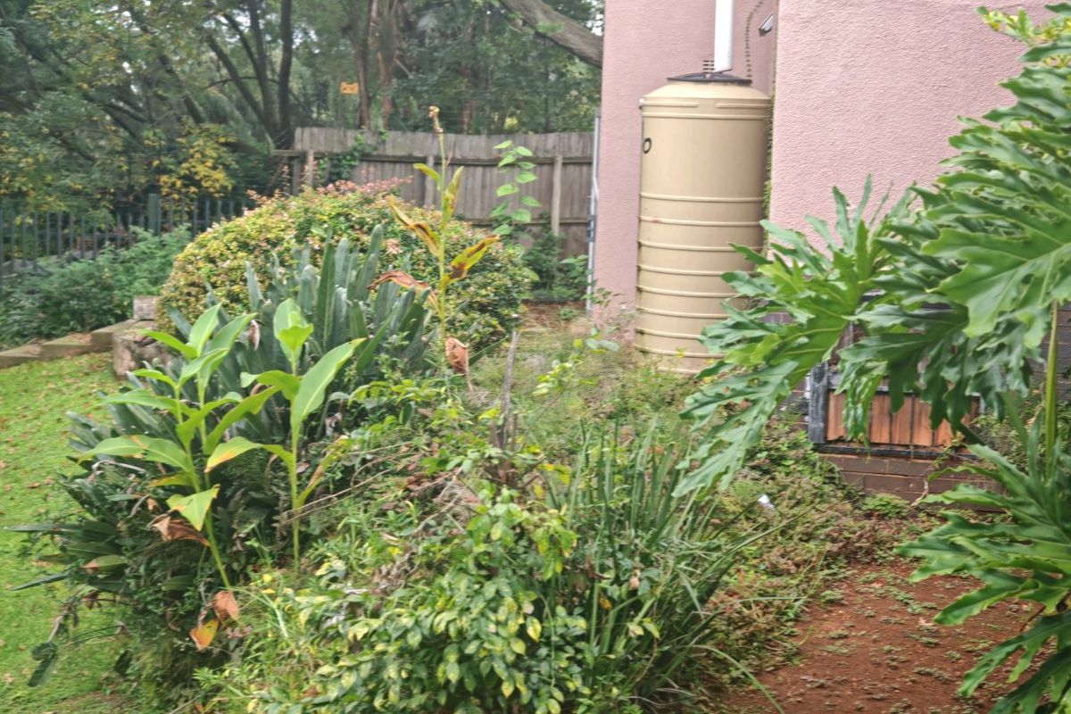 A view of the rear garden area featuring a large water storage tank and established garden beds against the property exterior.