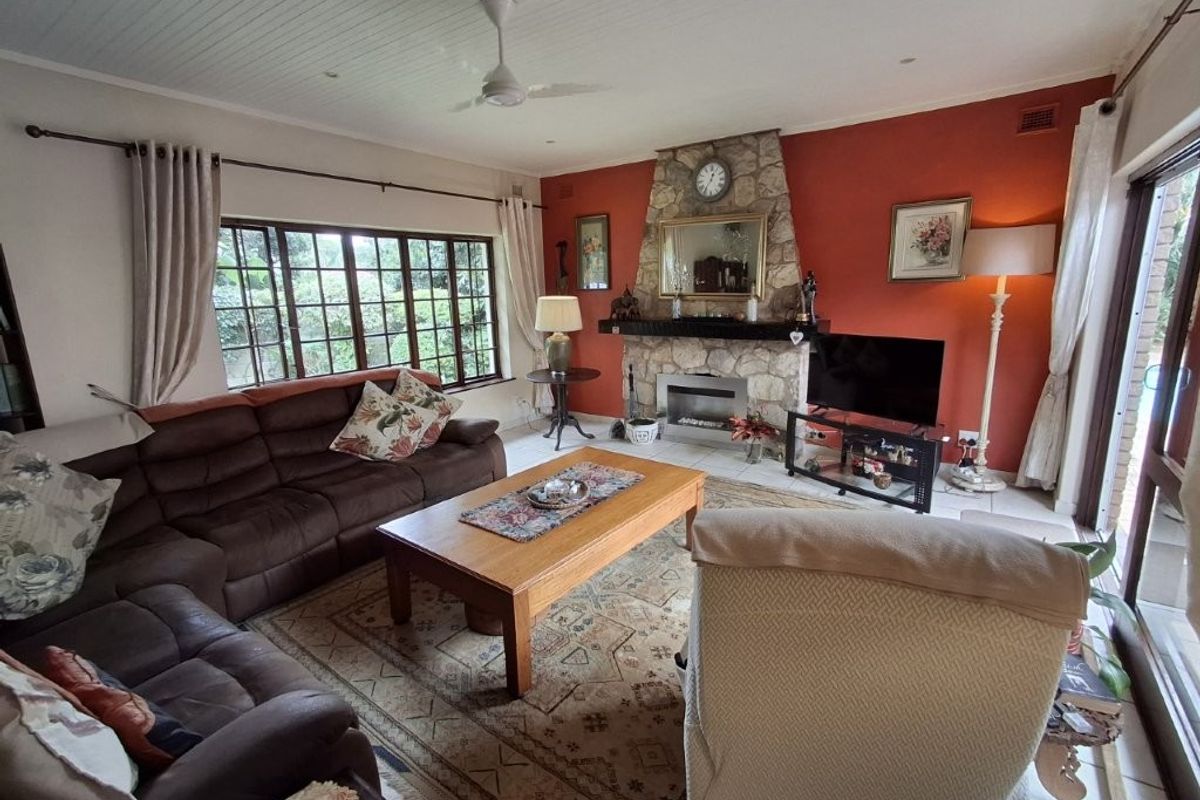 A cozy living room featuring a prominent stone fireplace, tiled flooring, and a ceiling fan, with large windows providing natural light.