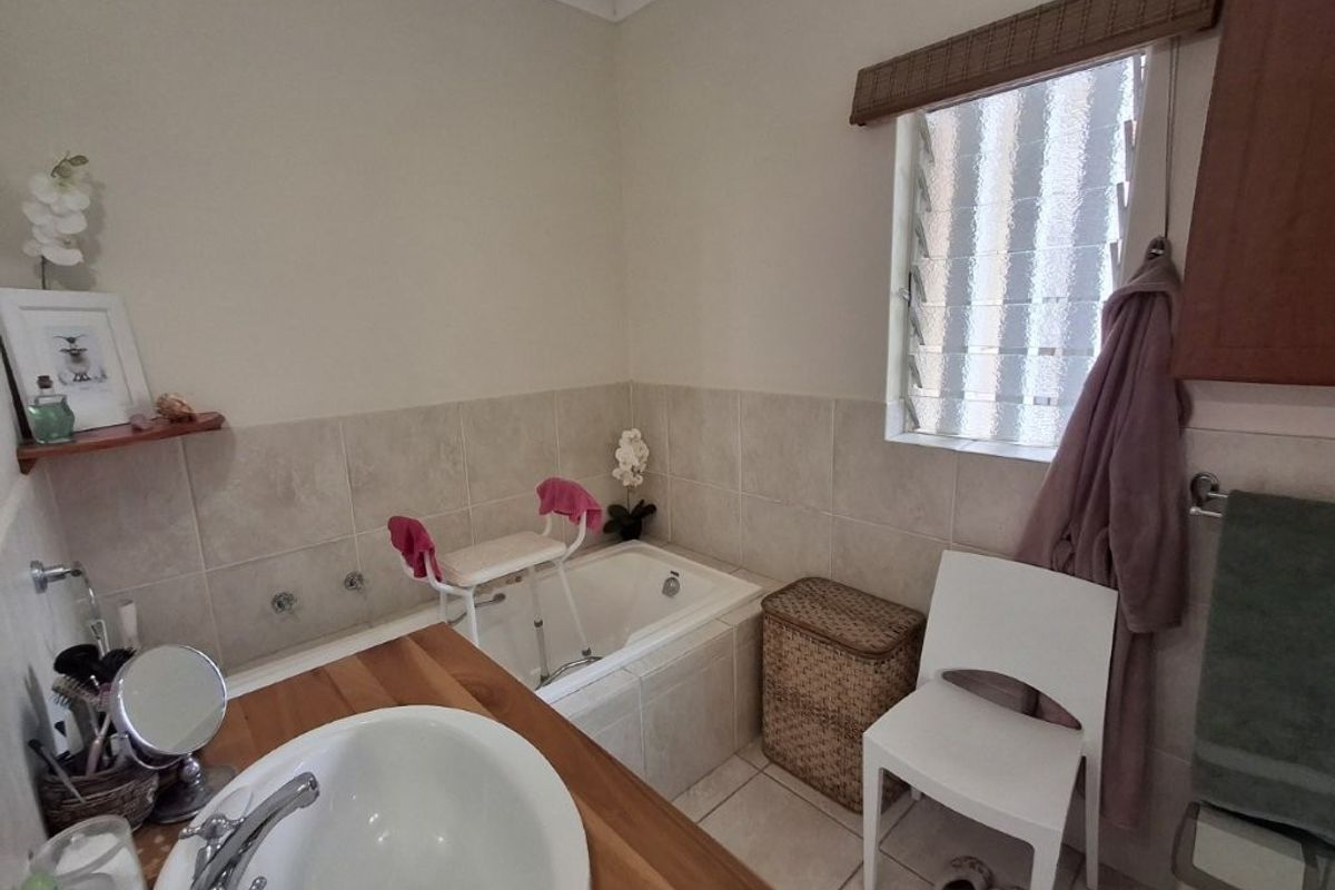 A functional bathroom featuring a built-in bathtub with tiled surround, a vanity basin with a wooden countertop, and a louvre window for ventilation.