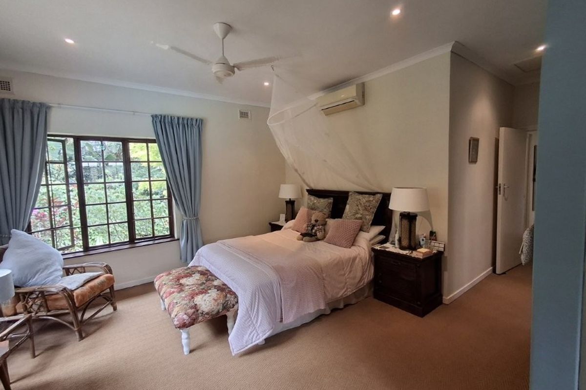 A well-proportioned bedroom featuring carpeted flooring, a ceiling fan, and a wall-mounted split-system air conditioner, with large windows overlooking the garden.