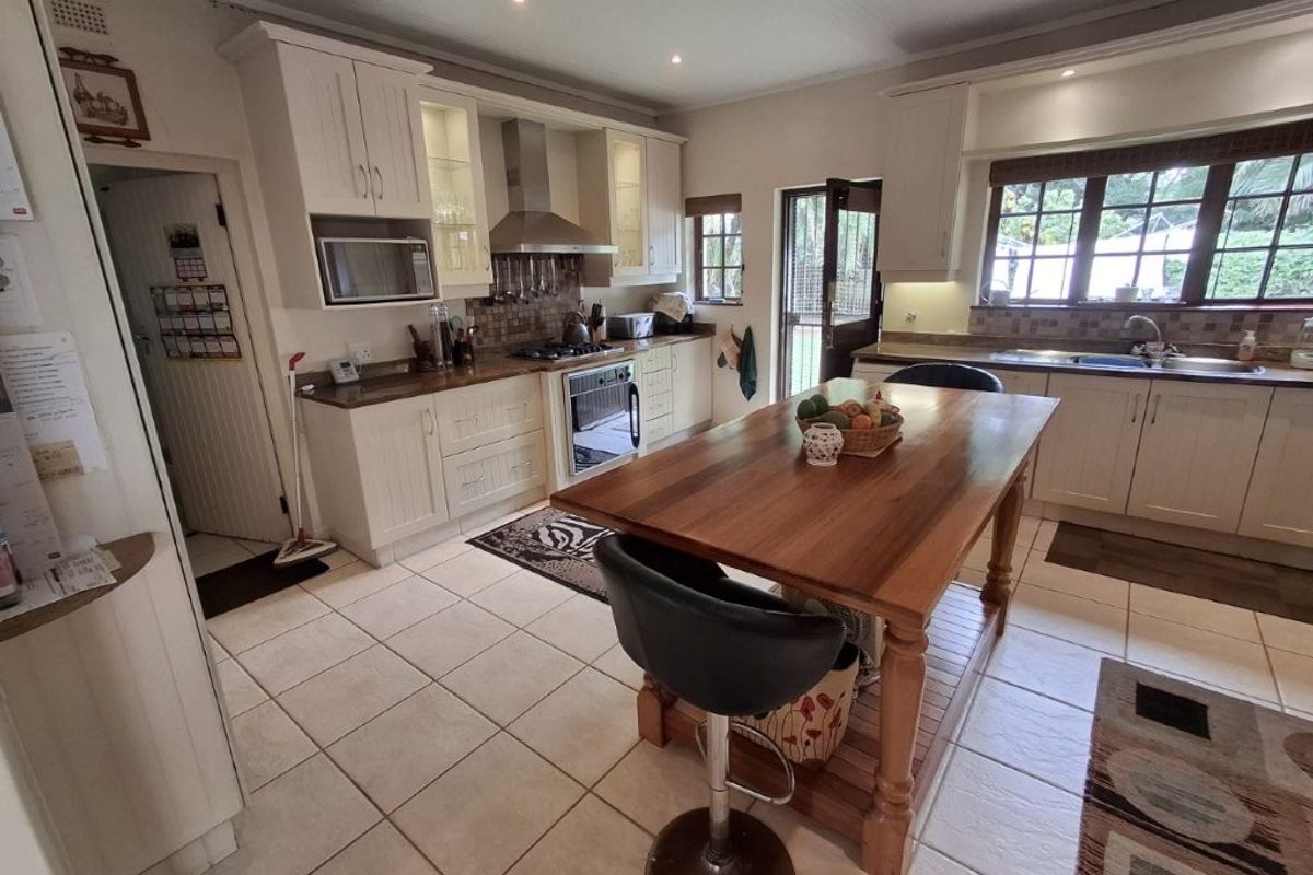 A well-maintained kitchen featuring cream cabinetry, wooden countertops, a central island, built-in appliances, and tiled flooring with direct access to the exterior.