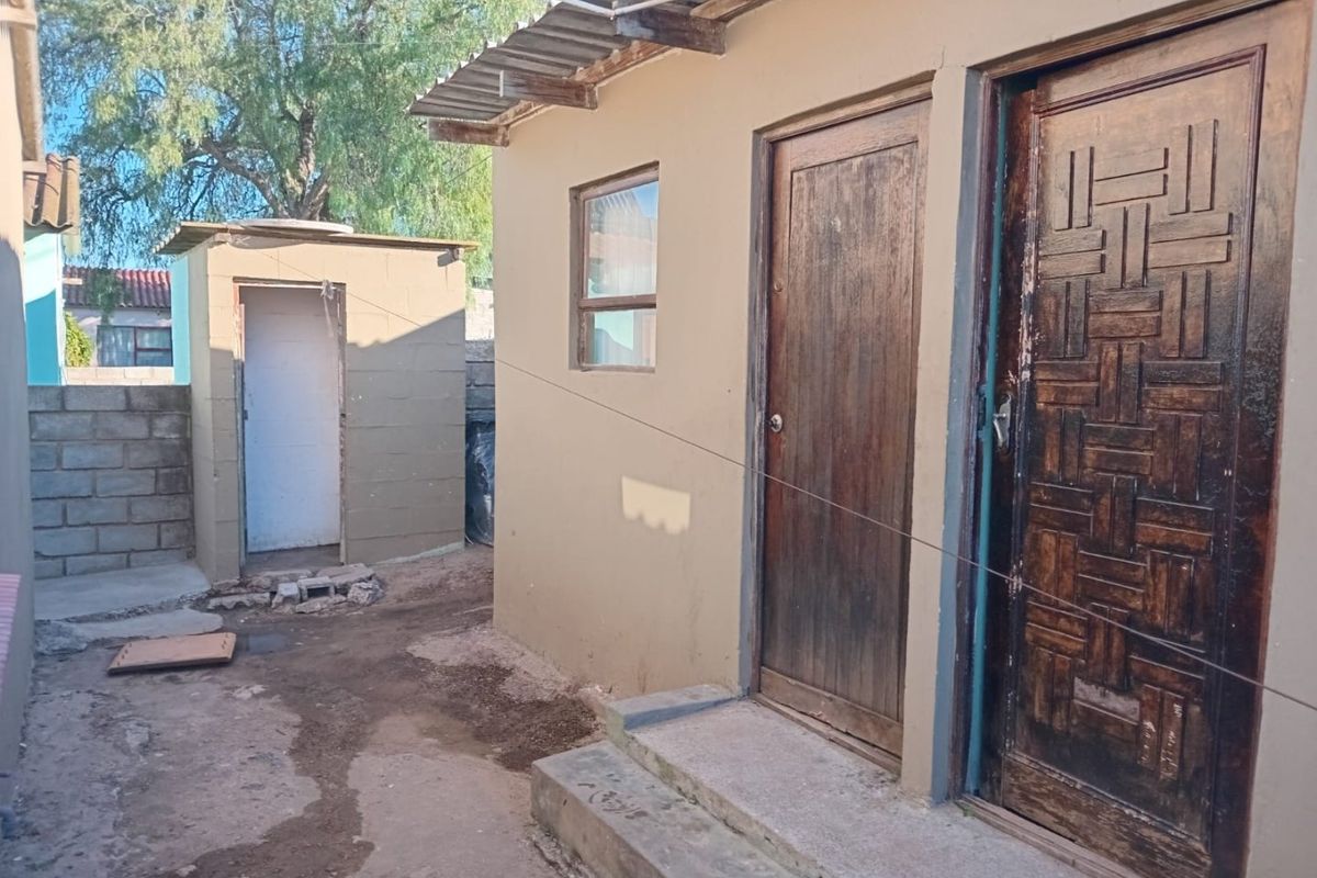Rear exterior view of the property showing a small outbuilding, concrete steps, and multiple timber entrance doors with visible wear to the exterior finishes.