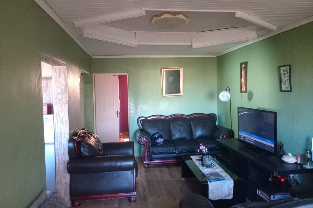 A living room featuring laminate flooring and a panelled ceiling, with access to adjacent rooms.