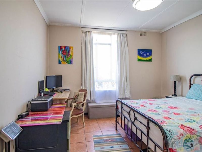 A bedroom featuring tiled flooring and a central window, requiring cosmetic updates to the wall and ceiling finishes to improve its overall condition.