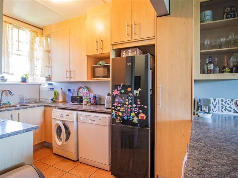 A functional kitchen featuring light wood-tone cabinetry, laminate countertops, tiled flooring, and integrated space for laundry appliances.