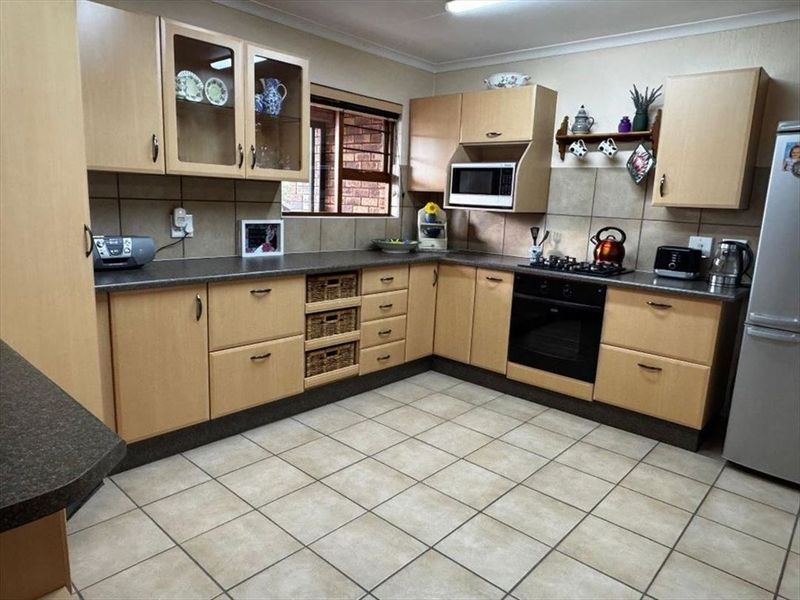 A functional kitchen featuring light wood-finish cabinetry, dark laminate countertops, a built-in oven with gas hob, and neutral tiled flooring.