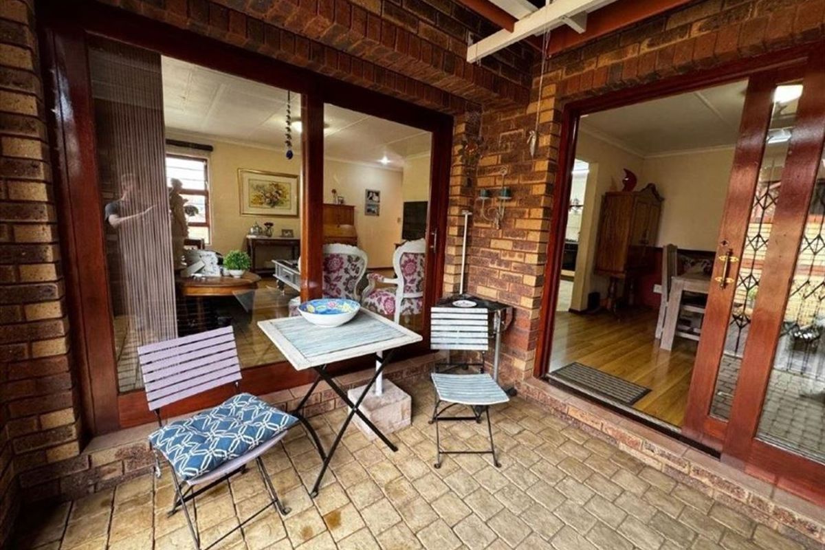A covered patio area featuring brick paving and exposed brick walls, providing direct access to the interior living spaces through timber sliding doors.
