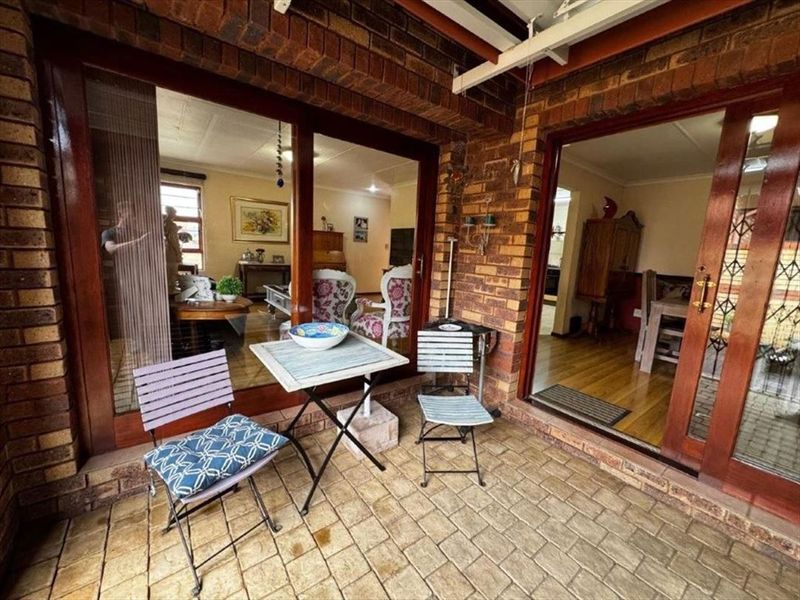 A covered patio area featuring brick paving and exposed brick walls, providing direct access to the interior living spaces through timber sliding doors.