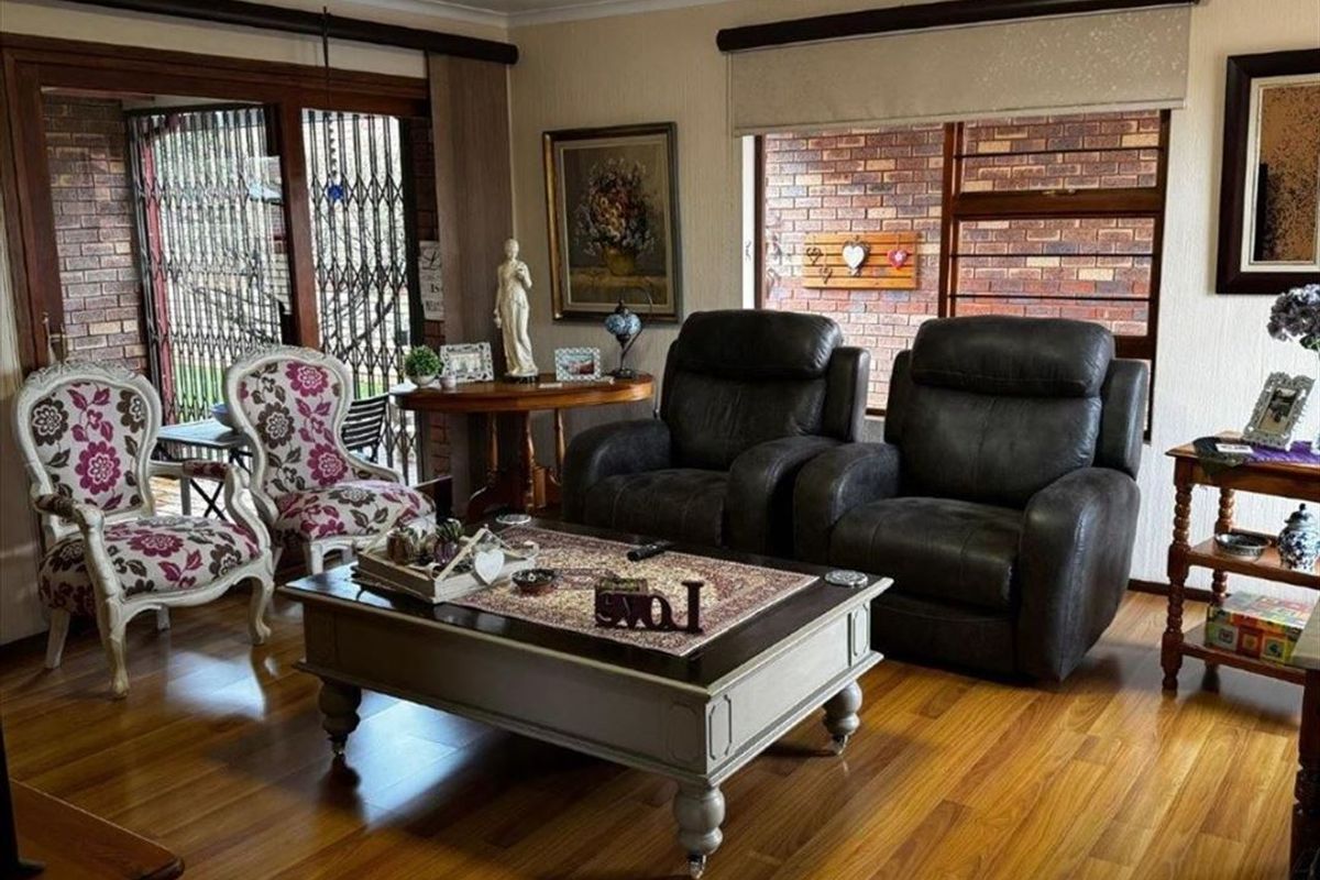 A cozy living room featuring warm laminate flooring, exposed brick feature walls, and large windows with roller blinds, providing a comfortable and inviting atmosphere.