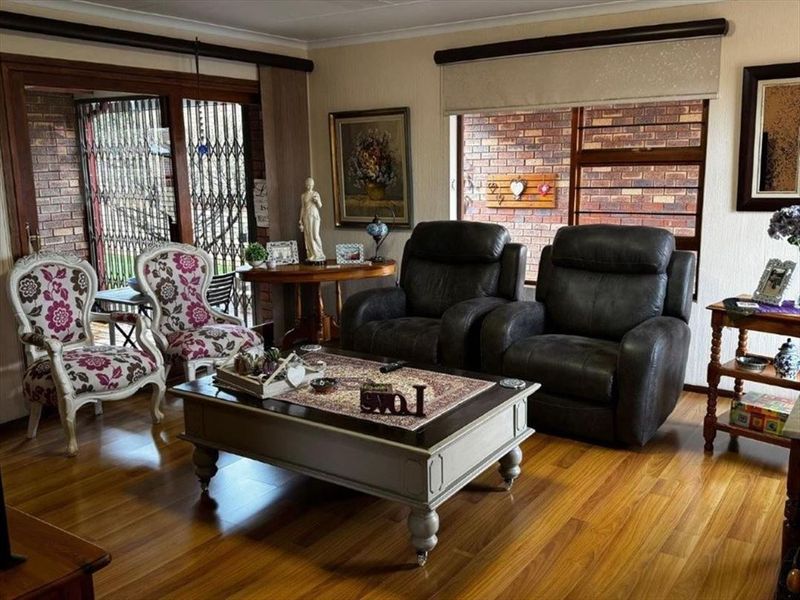 A cozy living room featuring warm laminate flooring, exposed brick feature walls, and large windows with roller blinds, providing a comfortable and inviting atmosphere.