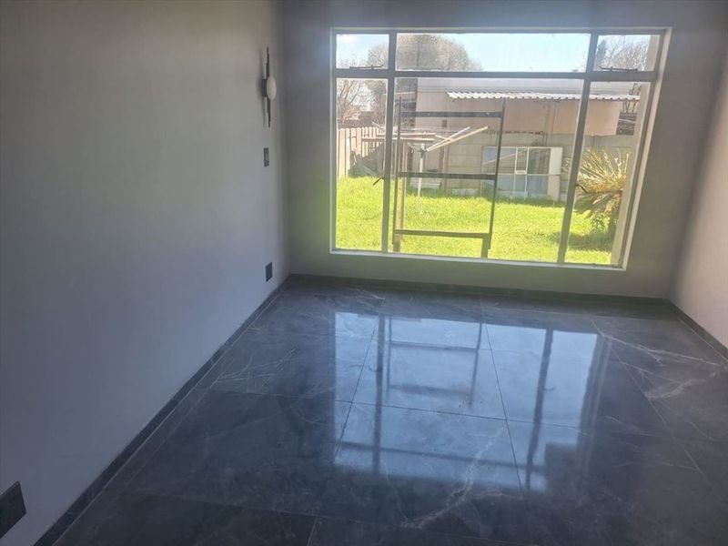 A bright, empty bedroom featuring polished grey marble-look floor tiles and a large window overlooking the rear garden.