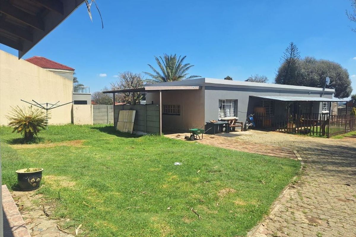 Rear view of the property featuring a paved driveway, lawn area, and a covered patio space with security bars on windows.
