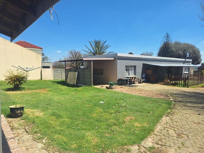 Rear view of the property featuring a paved driveway, lawn area, and a covered patio space with security bars on windows.