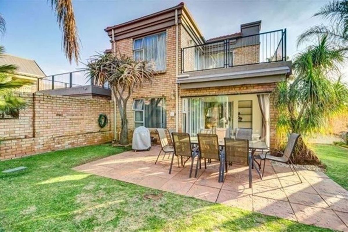 Rear view of a two-story brick house featuring a paved patio area, a balcony with metal railings, and a private garden space.
