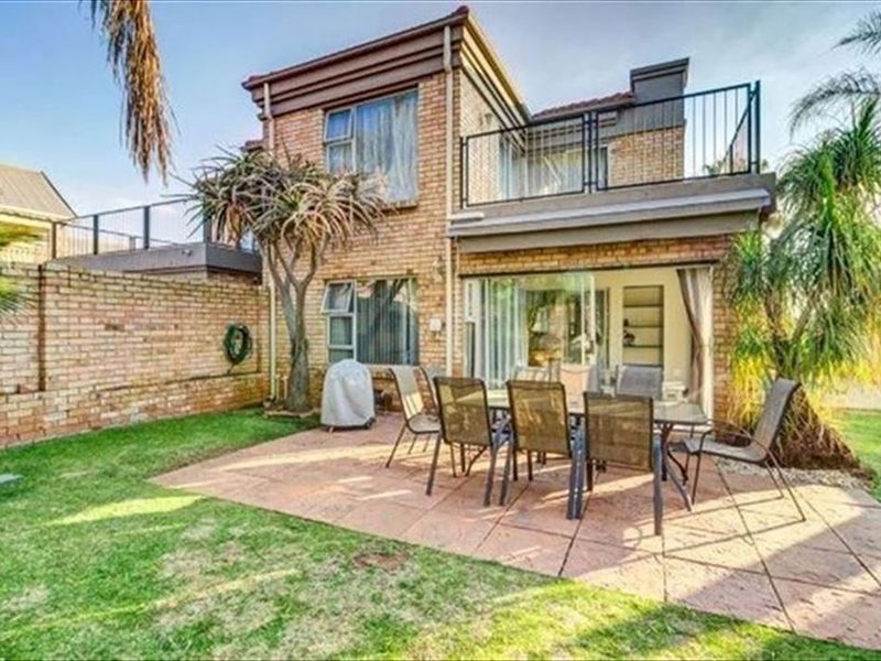 Rear view of a two-story brick house featuring a paved patio area, a balcony with metal railings, and a private garden space.