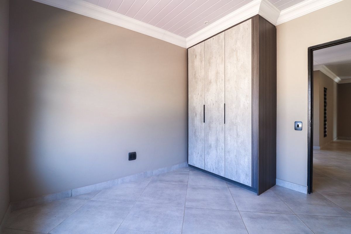 A clean, modern bedroom featuring neutral tiled flooring, built-in cupboards with contemporary finishes, and elegant crown molding.