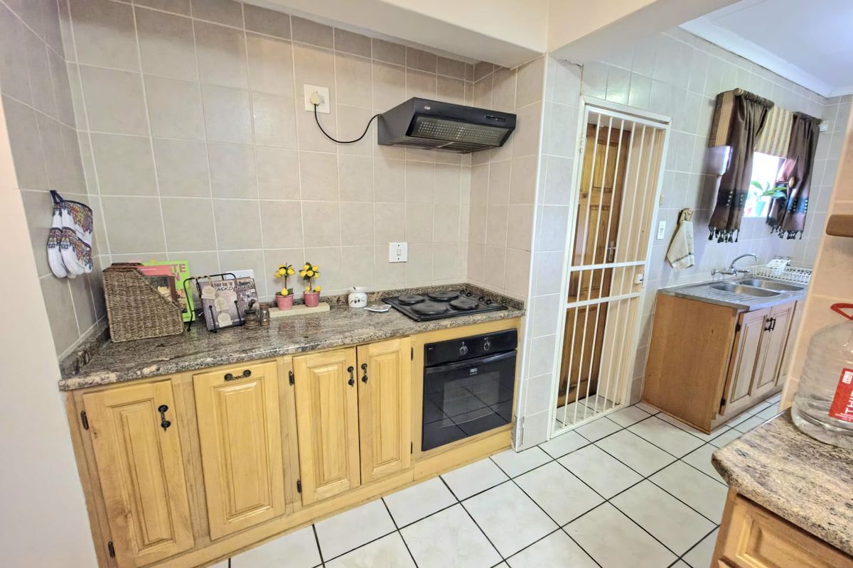 Functional kitchen featuring granite countertops, built-in oven, electric hob, extractor fan, and tiled splashbacks with traditional wooden cabinetry.