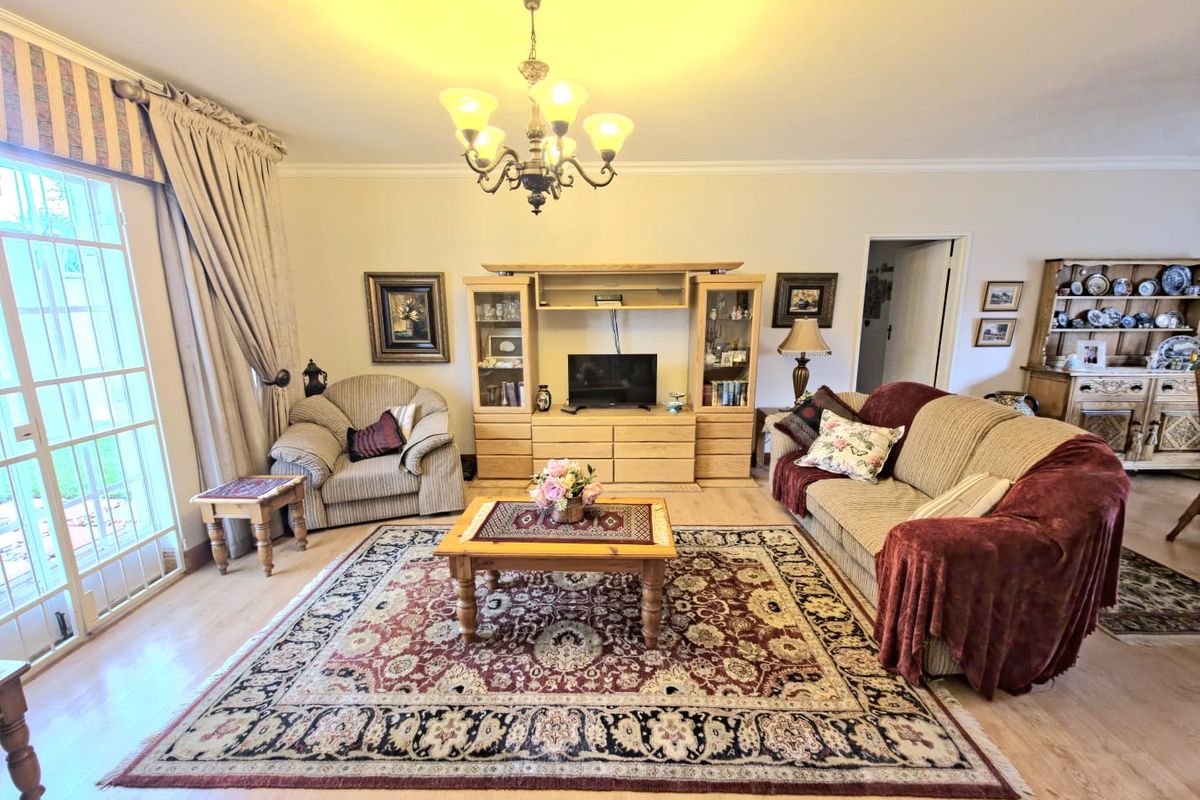 A spacious living room featuring laminate flooring, a central chandelier, and a built-in entertainment unit, with direct access to the outdoor area via sliding doors.