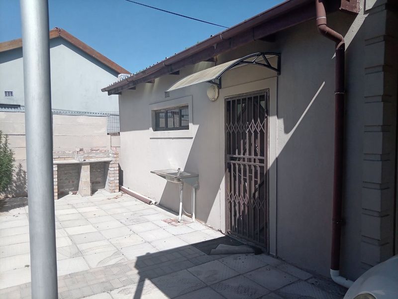 Rear exterior area featuring a paved patio, built-in brick braai, and a stainless steel utility sink with security gate access.