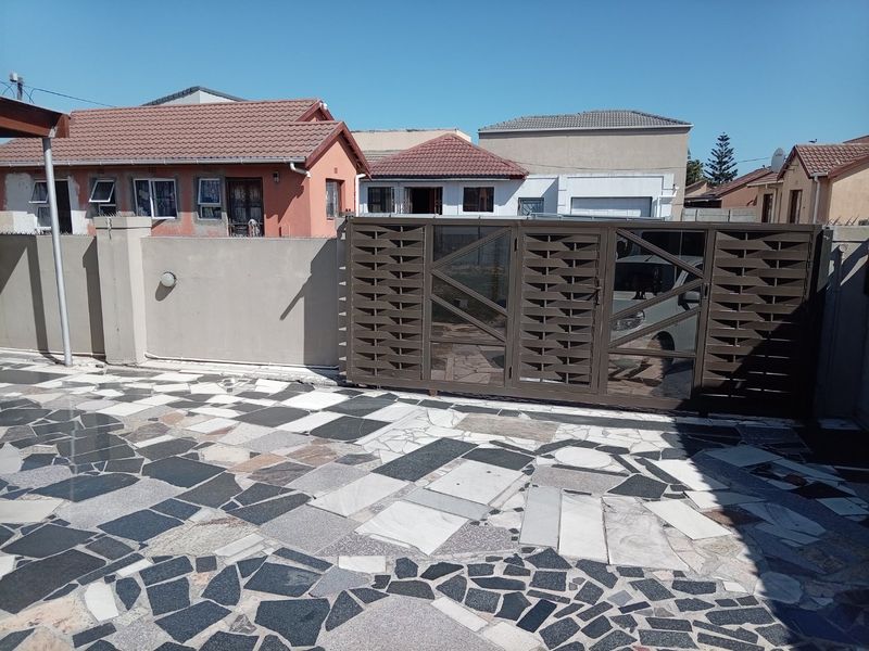 Front exterior view featuring a modern metal sliding gate, a solid boundary wall, and a decorative paved driveway area.