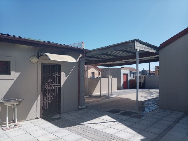 Rear exterior area featuring a paved patio, a covered carport structure, and an external utility sink with security gate access.