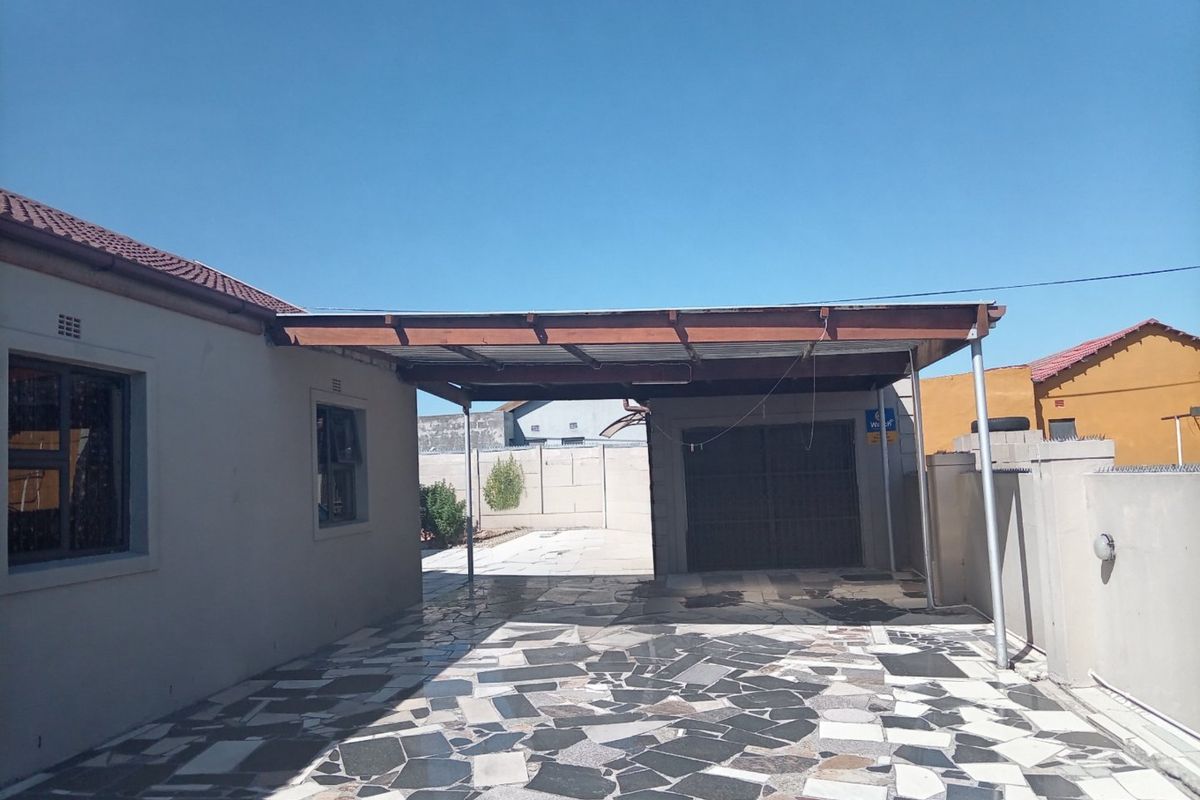 Rear exterior area featuring a paved patio, a covered carport structure, and a secure garage entrance.
