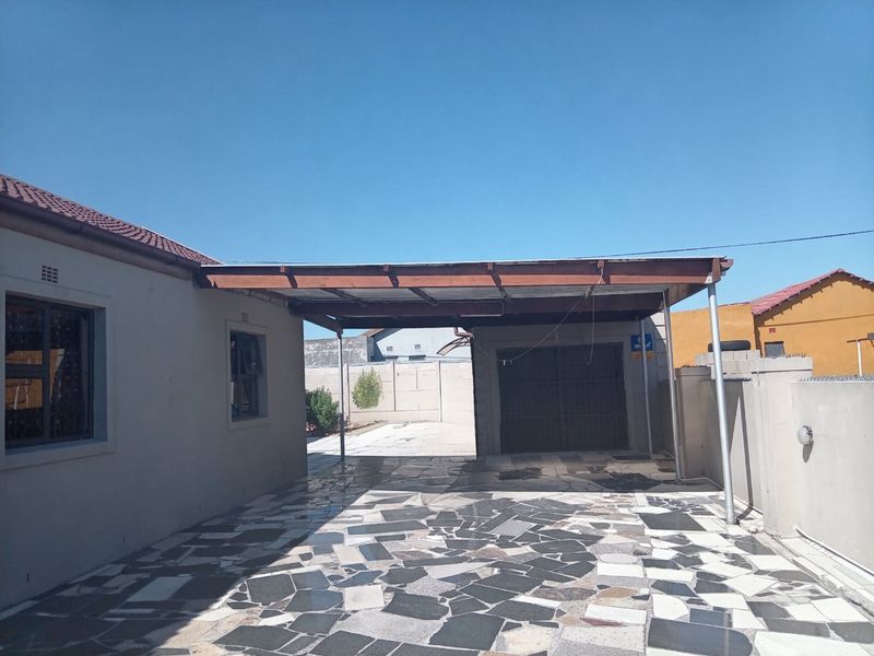 Rear exterior area featuring a paved patio, a covered carport structure, and a secure garage entrance.