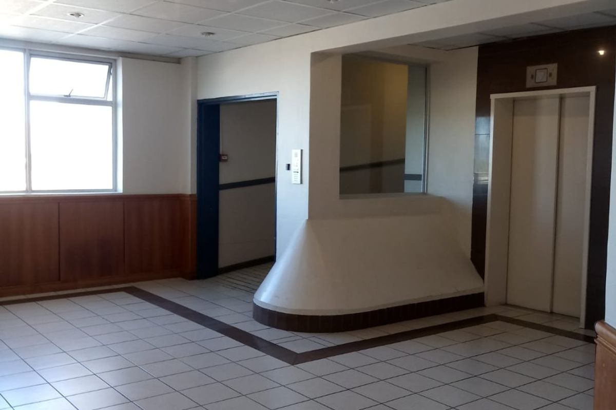 A spacious apartment building entrance lobby featuring tiled flooring, timber wall paneling, a suspended ceiling, and elevator access.
