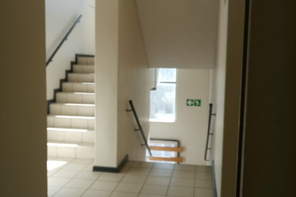 A functional apartment building hallway featuring tiled flooring, a staircase with handrails, and standard recessed ceiling lighting.