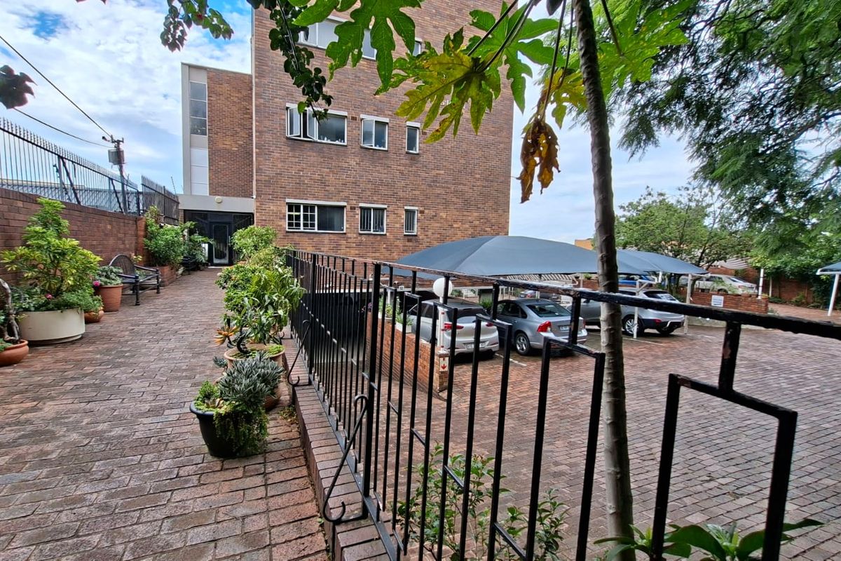 Exterior view of the apartment complex featuring a brick facade, paved walkway, and covered parking area with shade cloth structures.