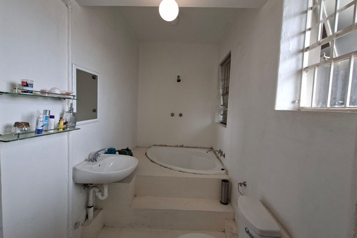 A dated bathroom featuring a raised corner bathtub, a wall-mounted basin, and a toilet, with potential for modernization and cosmetic updates.