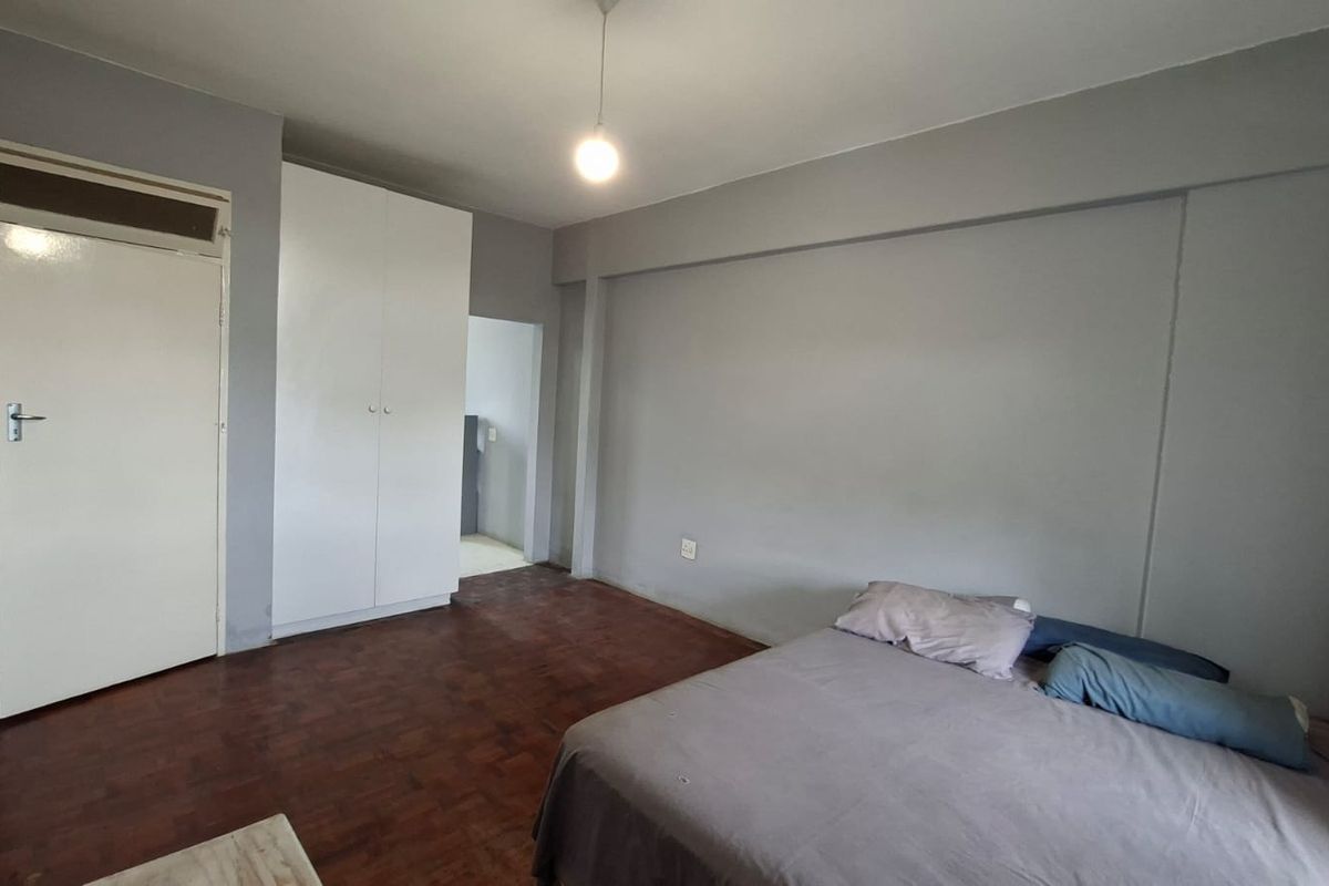 A bedroom featuring parquet flooring, built-in cupboards, and a neutral grey color scheme, offering a functional and simple living space.