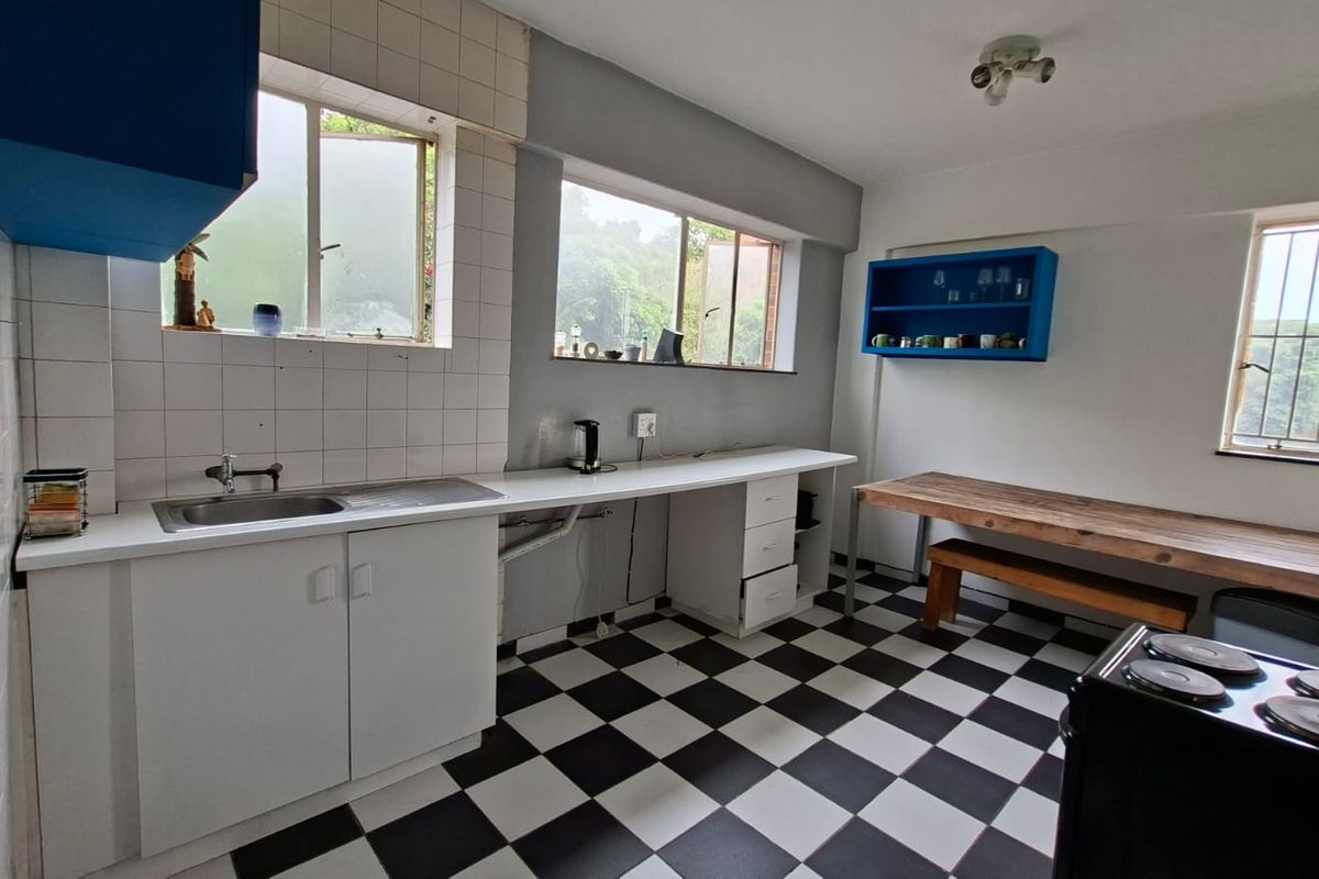 A functional kitchen featuring a stainless steel sink, tiled splashbacks, checkerboard flooring, and ample counter space with built-in cabinetry.
