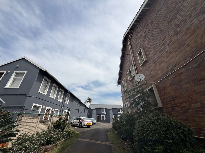 Exterior view of the apartment complex showing brick and painted masonry facades, paved driveway access, and established boundary landscaping.