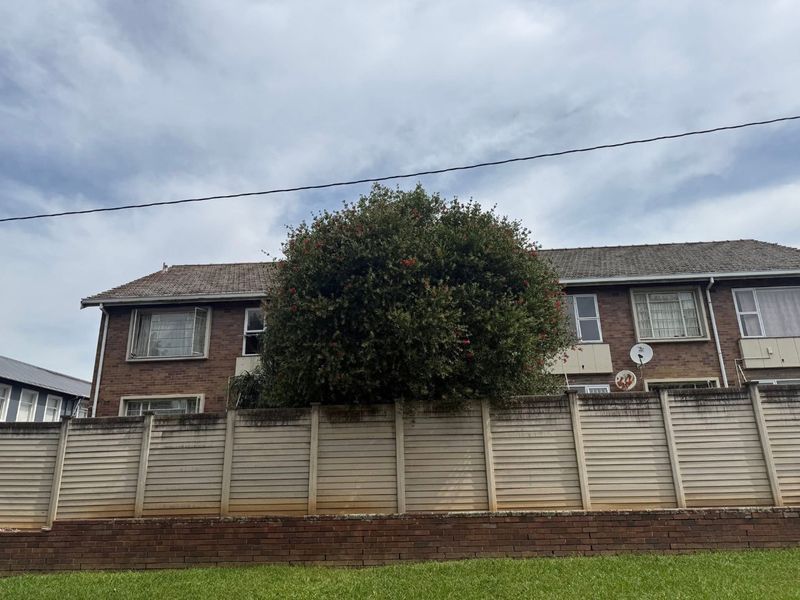 Rear view of a brick apartment building featuring a precast concrete boundary wall and a tiled roof.