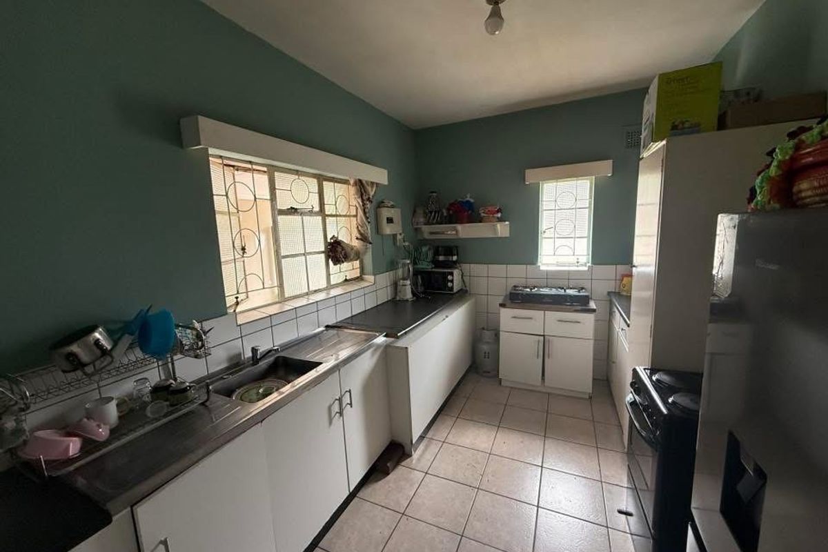 A functional kitchen featuring tiled flooring, a stainless steel sink, built-in cabinetry, and a tiled backsplash with security bars on the windows.