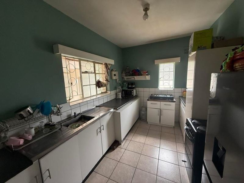 A functional kitchen featuring tiled flooring, a stainless steel sink, built-in cabinetry, and a tiled backsplash with security bars on the windows.