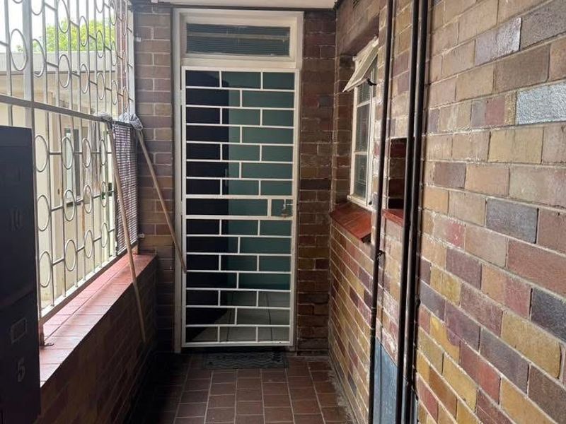 A secure apartment entrance featuring brick walls, tiled flooring, and a protective security gate.