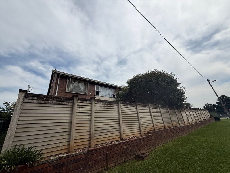 Exterior view of the property featuring a brick retaining wall and a precast concrete boundary wall with security spikes.