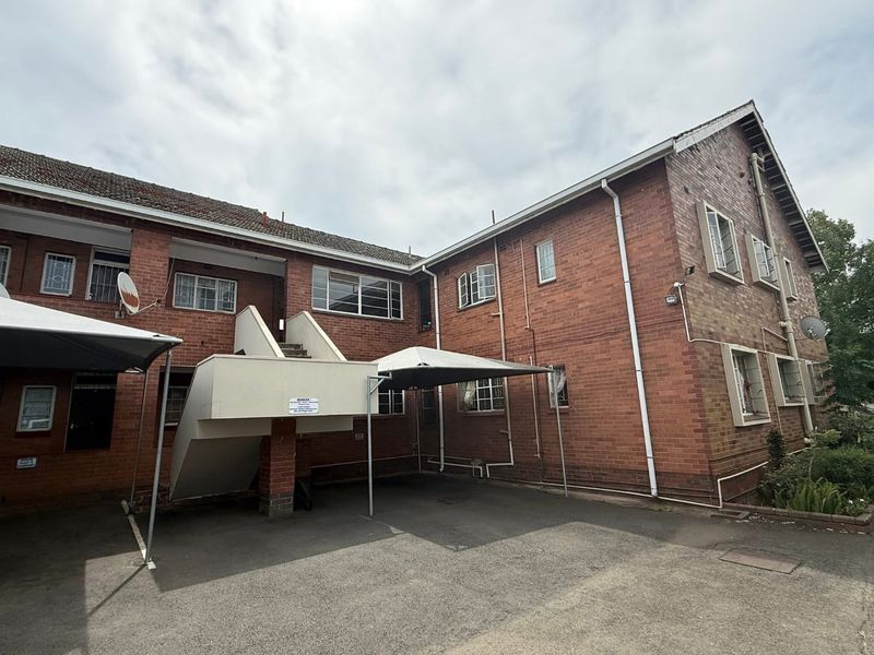 Exterior view of a brick apartment building featuring a covered carport, external staircase, and security-fitted windows.