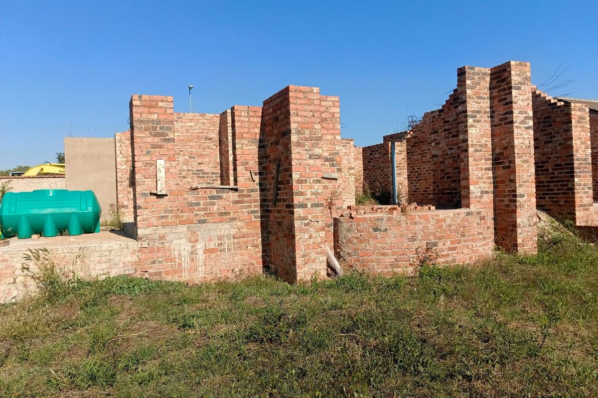 An unfinished residential construction site showing exposed brick walls and a water storage tank on a vacant plot.