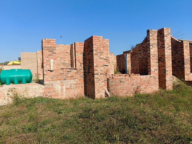 An unfinished residential construction site showing exposed brick walls and a water storage tank on a vacant plot.