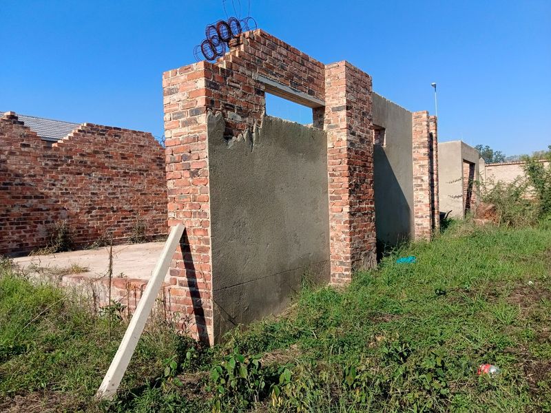 An unfinished construction site showing exposed brick walls, concrete foundations, and structural elements in the early stages of development.