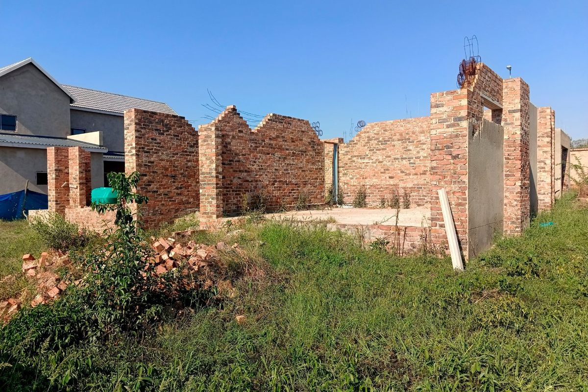 An unfinished residential construction site showing exposed brick walls and a concrete foundation slab in a suburban setting.
