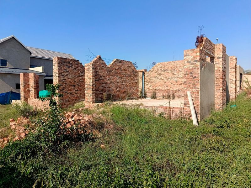 An unfinished residential construction site showing exposed brick walls and a concrete foundation slab in a suburban setting.