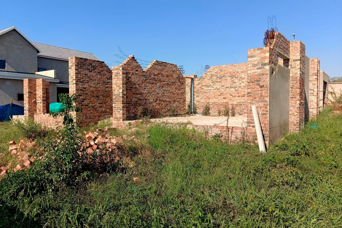 An unfinished residential construction site showing exposed brick walls and a concrete foundation slab, currently in the early stages of development.